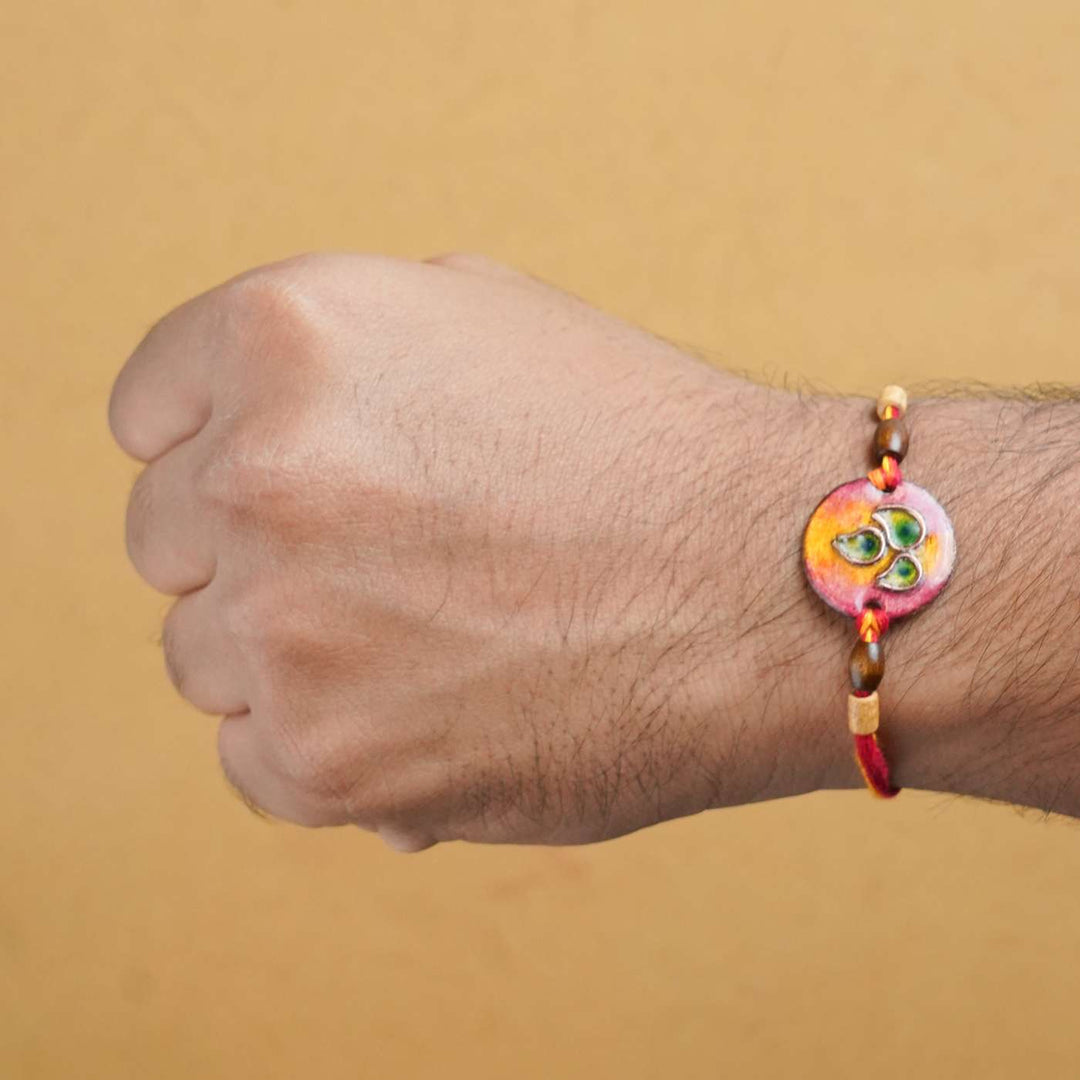 Handmade Morpankh Copper Enamel Rakhi With Chocolates And Roli Chawal - Red bracelet worn on wrist