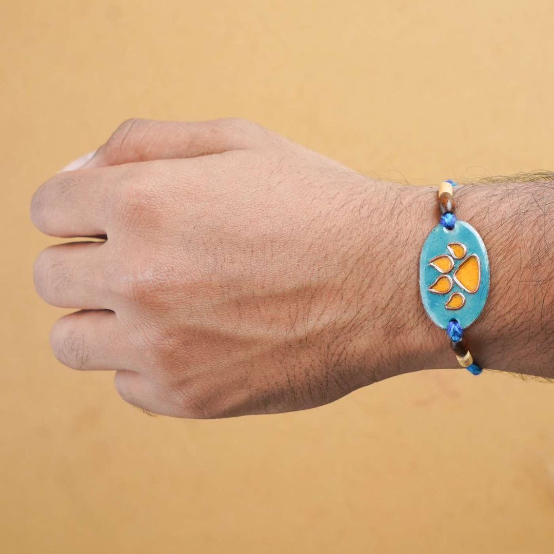 Handmade Pawfect Copper Enamel Rakhi With Chocolates And Roli Chawal - Orange Paw Charm on Wrist