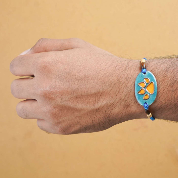 Handmade Pawfect Copper Enamel Rakhi With Chocolates And Roli Chawal - Orange Paw Charm on Wrist