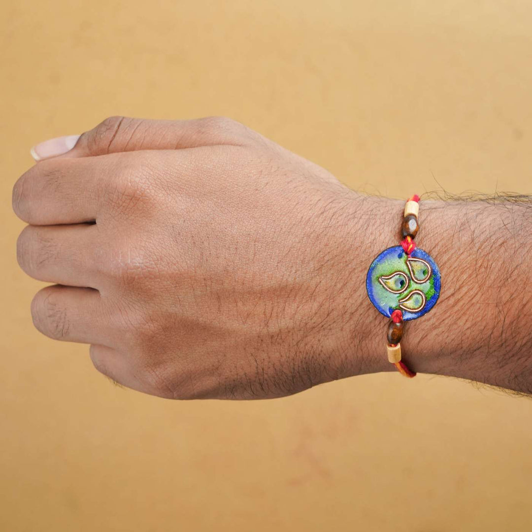 Handmade Morpankh Copper Enamel Rakhi With Chocolates And Roli Chawal - Blue bracelet worn on wrist
