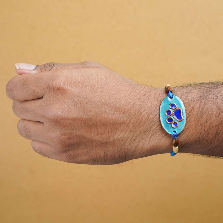 Handmade Pawfect Copper Enamel Rakhi With Chocolates And Roli Chawal - Blue Paw Charm on Wrist
