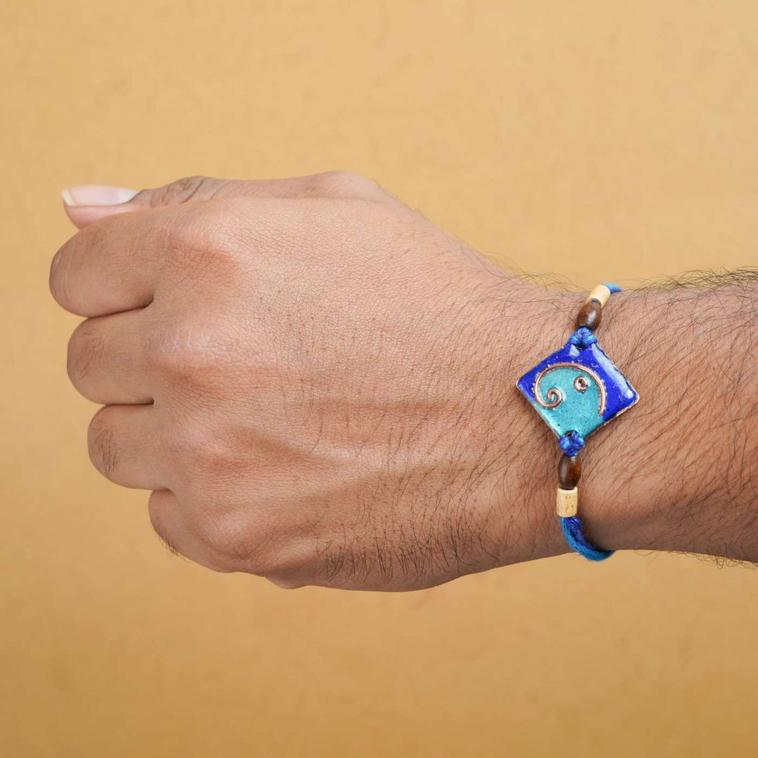 Handmade Square Ganesh Copper Enamel Rakhi With Chocolates And Roli Chawal - Blue rakhi worn on wrist