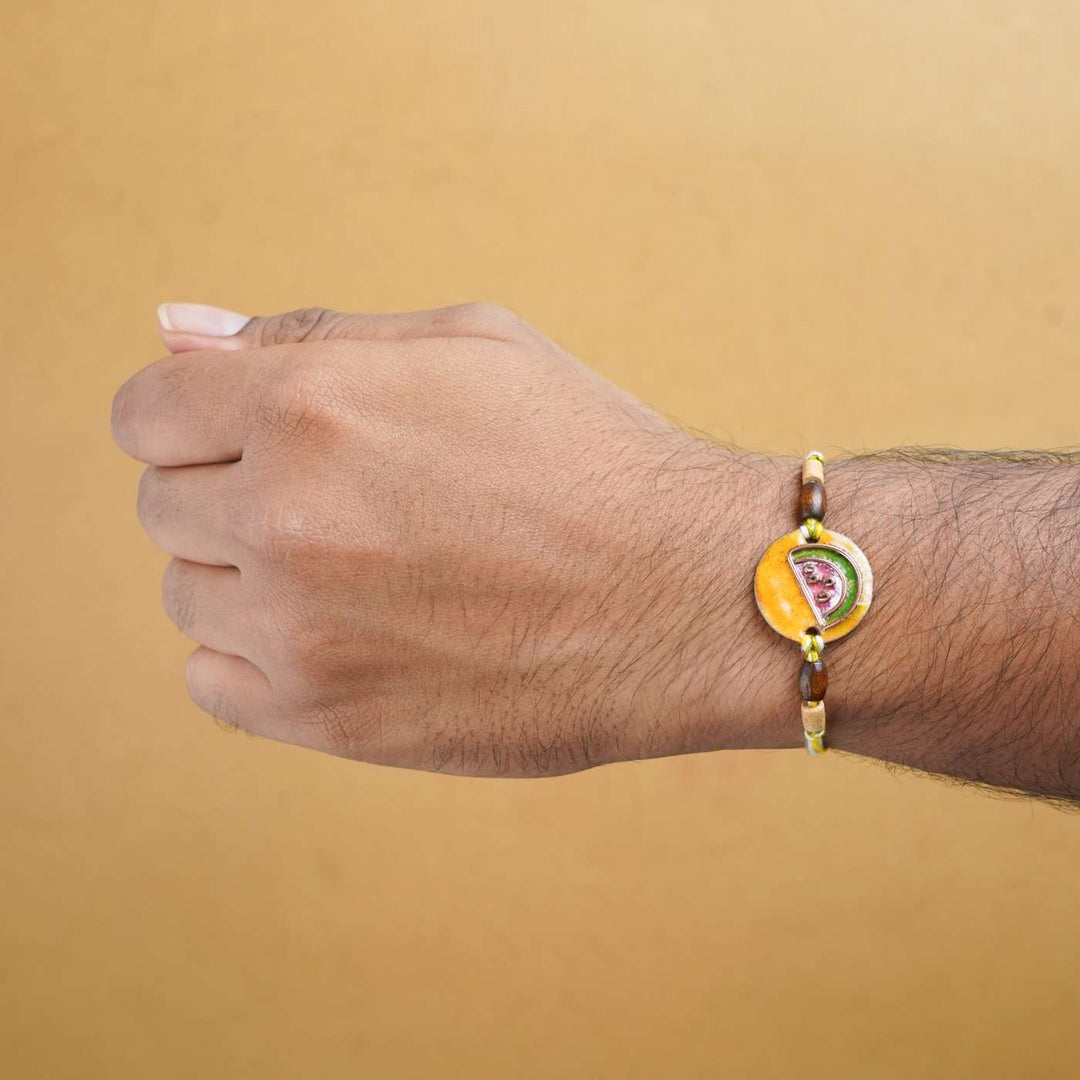 Handmade Tarbooz Red Copper Enamel Rakhi With Chocolates And Roli Chawal - Rakhi worn on wrist