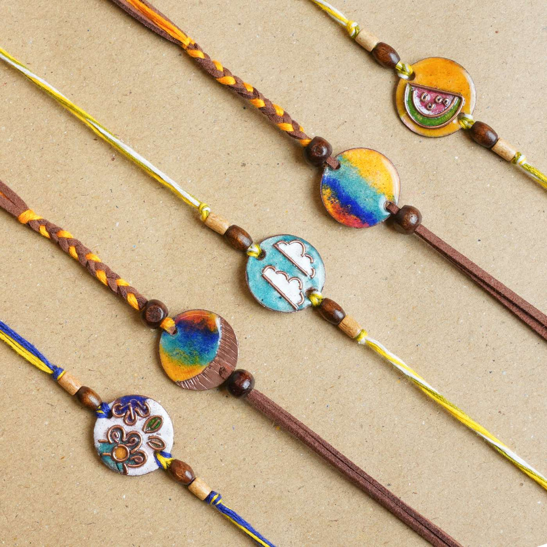 Handmade Square Ganesh Copper Enamel Rakhi With Chocolates And Roli Chawal - Flat lay of assorted rakhis