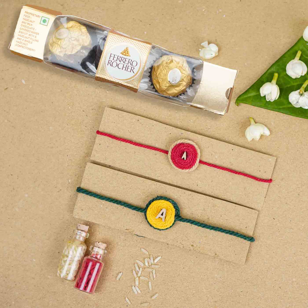 Personalized Handmade Alphabet Cotton Rakhi With Roli Chawal Set Of 2 - Flat Lay with Packaging and Chocolates