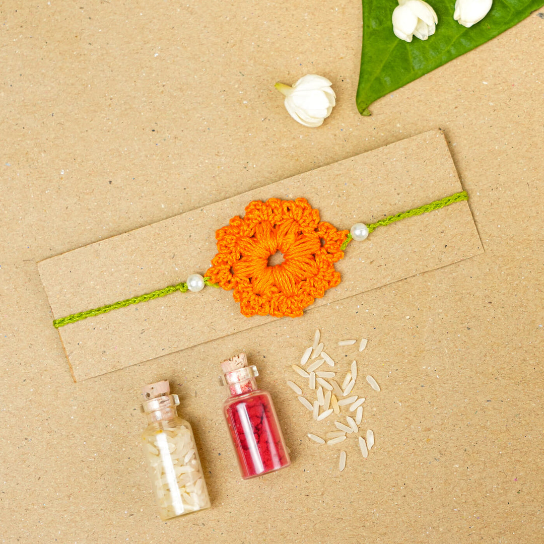 Handmade Crochet Floral Cotton Rakhi With Roli Chawal - Orange Rakhi on packaging board