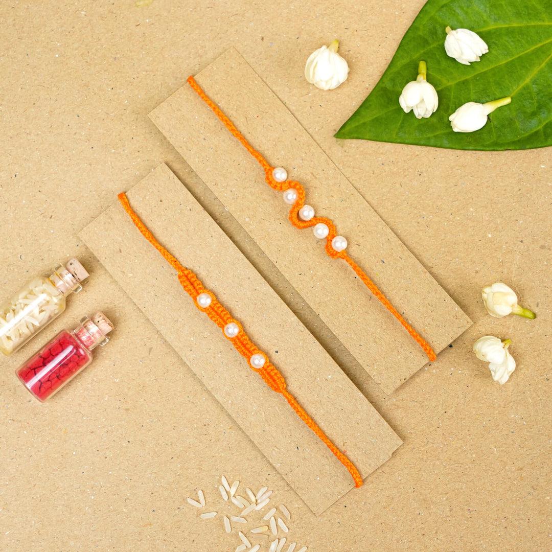 Handmade Macrame Beaded Rakhi With Roli Chawal Set Of 2 1 - Orange rakhis on cardboard