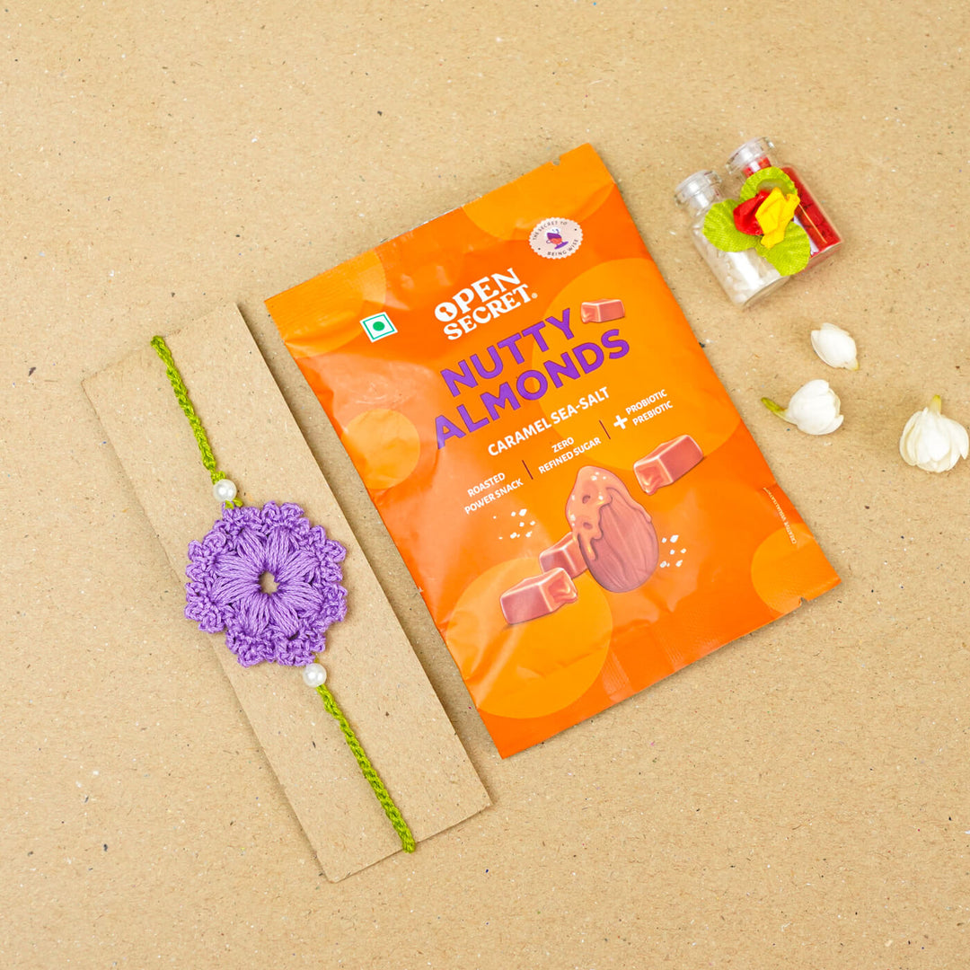 Handmade Crochet Floral Cotton Rakhi With Roli Chawal - Flat lay with gift snack