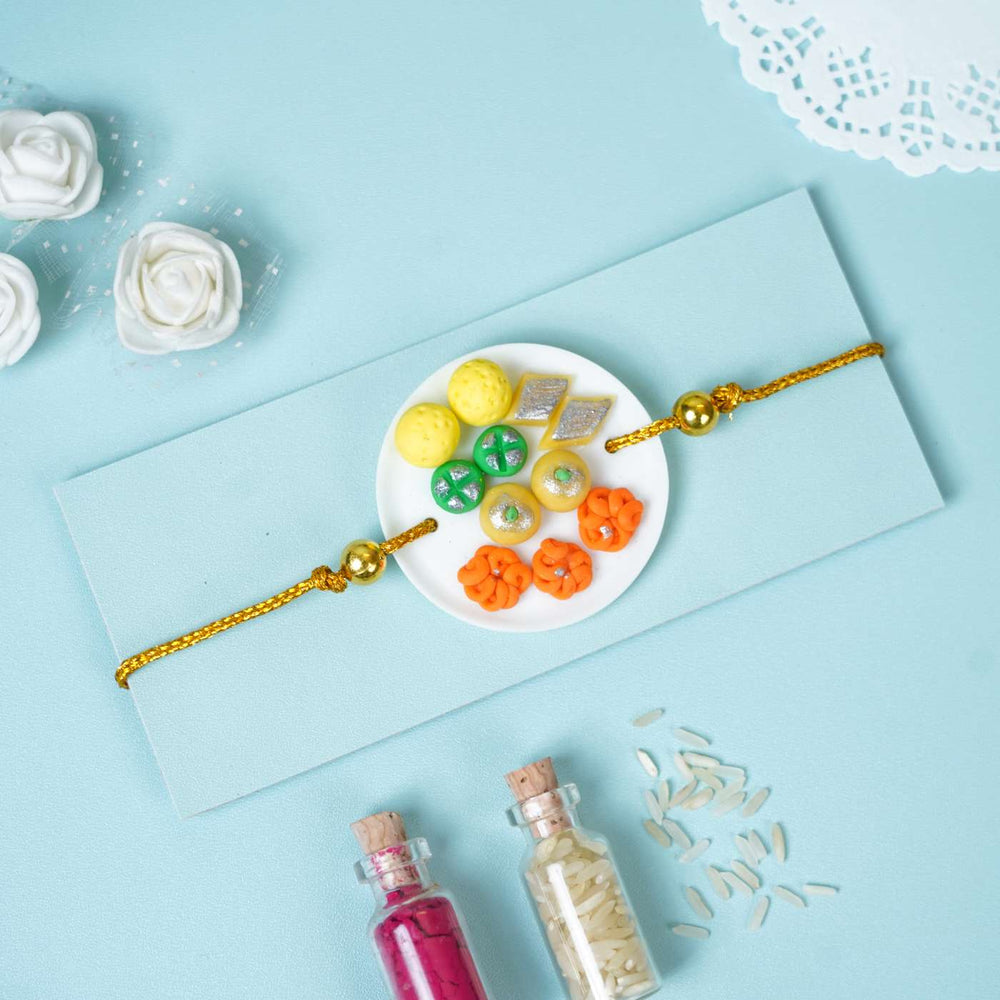 Handmade Miniature Clay Traditional Sweets Rakhi With Roli Chawal - Flat lay showing Rakhi on envelope