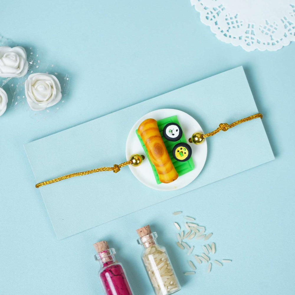 Handmade Miniature Clay Dosa Rakhi With Roli Chawal - Flat Lay with Card and Bottles