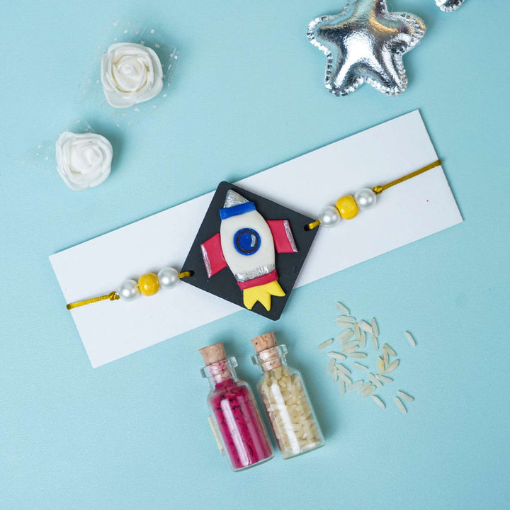 Handmade Miniature Clay Space Rocket Kids Rakhi With Roli Chawal - Flat Lay with Decorative Items
