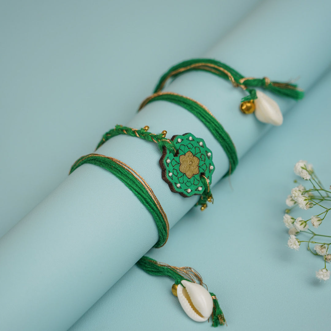 Handmade Green Flower Shape Ghungroo And Shell Wooden Bhaiya Bhabhi Rakhi With Roli Chawal - Wrapped on Cylinder Display