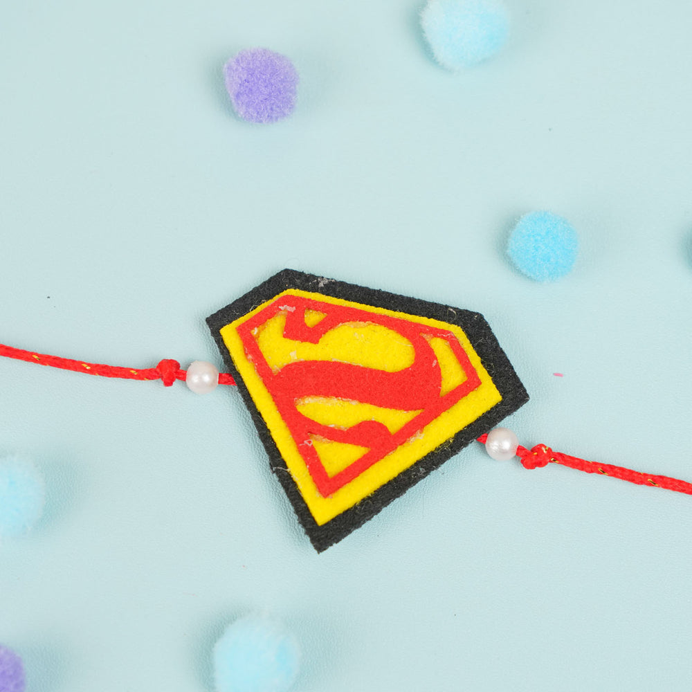 Handmade Beaded Superman Theme Pom Pom Felt Rakhi With Roli Chawal For Kids - Top-down view of Rakhi