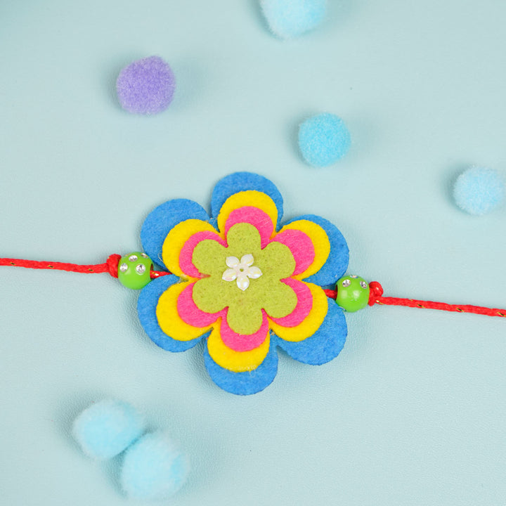 Handmade Beaded Flower Theme Pom Pom Felt Rakhi With Roli Chawal For Kids - Centered Flat Lay View