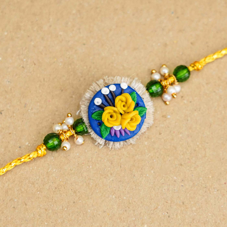 Handmade Miniature Clay Yellow And Blue Floral Rakhi With Roli Chawal - Close-up of bracelet centerpiece