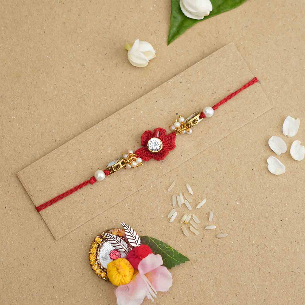 Handmade Kundan Floral Red Rakhi With Roli Chawal - Flat lay on cardboard backing