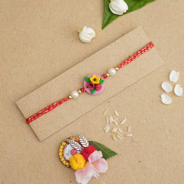 Handmade Miniature Clay Yellow And Red Floral Rakhi With Roli Chawal - Flat lay with decorative elements