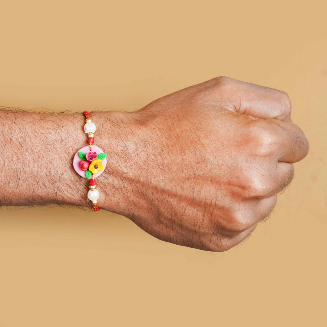 Handmade Miniature Clay Yellow And Red Floral Rakhi With Roli Chawal - Wrist view on person
