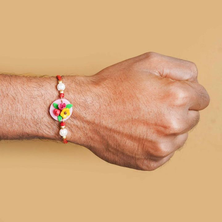 Handmade Miniature Clay Yellow And Red Floral Rakhi With Roli Chawal - Wrist view on person