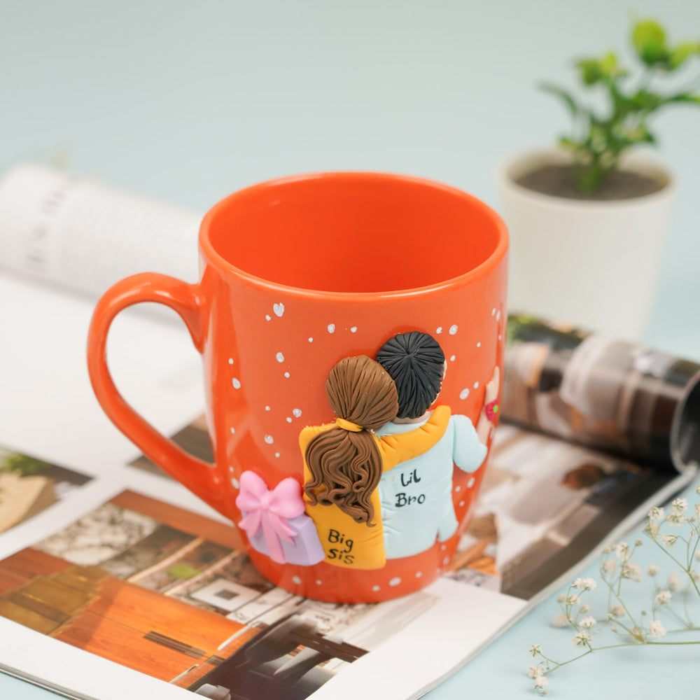 Handmade Big Sis And Lil Bro Clay Rakhi Hamper With Roli Chawal Includes 1 Mug 1 Rakhi - Mug Front Angle on Open Book