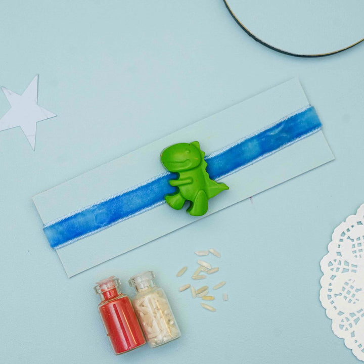 Handmade Dino Crayon Kids Rakhi With Roli Chawal - Flat lay with green dinosaur charm