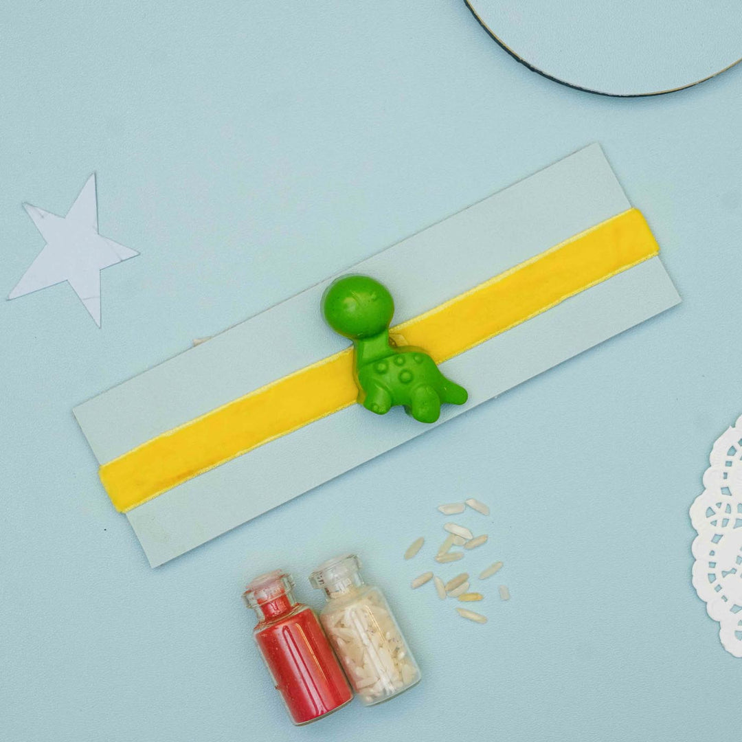 Handmade Dino Crayon Kids Rakhi With Roli Chawal - Flat lay with green dinosaur charm variant