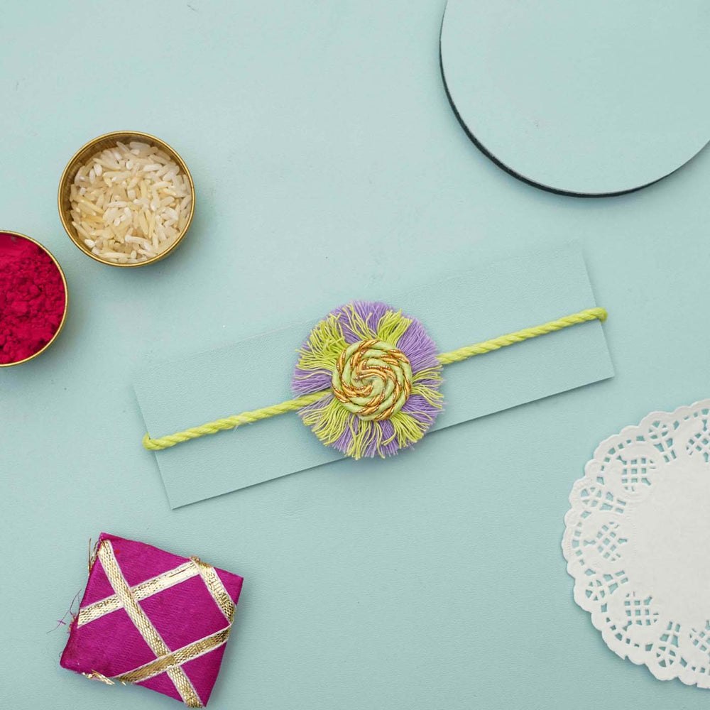 Handmade Macrame Purple And Green Cotton Rakhi With Chocolates And Roli Chawal - Flat lay with rakhi on card