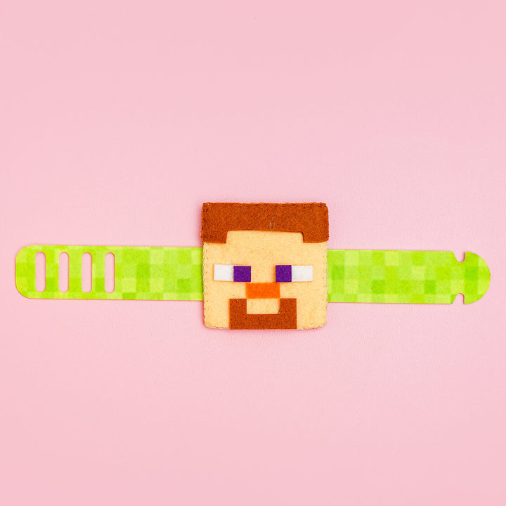 Handcrafted Minecraft Felt Rakhi For Kids With Roli Chawal - Laid Flat on Pink Surface