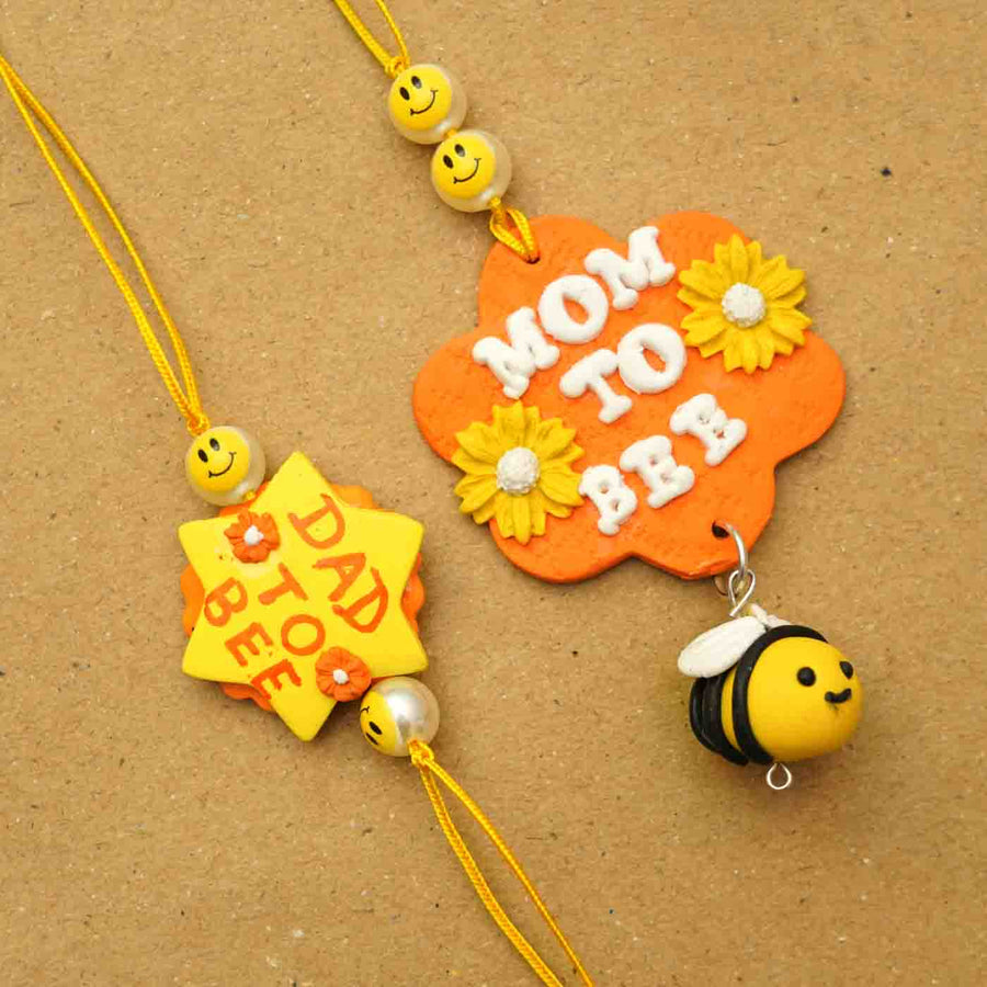 Handmade Parents To Be Clay Bhaiya Bhabhi Rakhi With Chocolates And Roli Chawal Set Of 2 - Close-up of two Rakhi designs