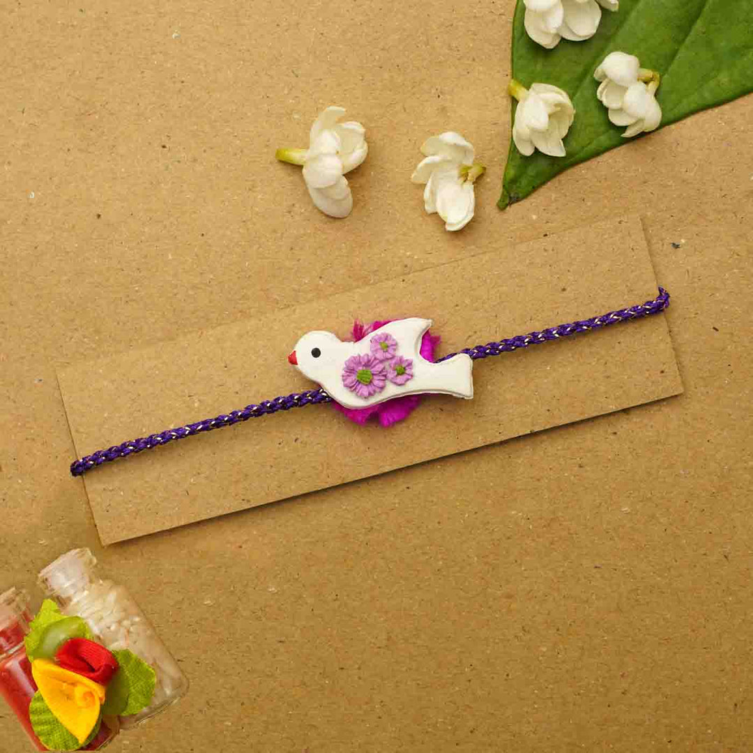 Handmade Bird Clay Rakhi With Chocolates Roli Chawal - Flat lay on packaging card