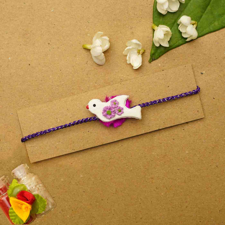 Handmade Bird Clay Rakhi With Chocolates Roli Chawal - Flat lay on packaging card