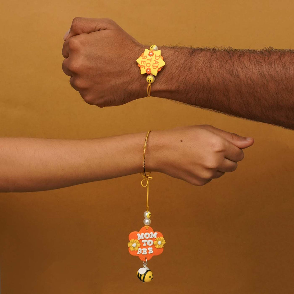 Handmade Parents To Be Clay Bhaiya Bhabhi Rakhi With Chocolates And Roli Chawal Set Of 2 - Hands wearing Dad To Bee and Mom To Bee Rakhi