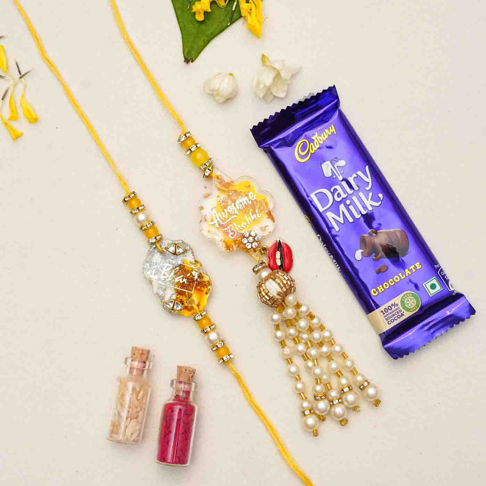 Handmade Resin Bhai And Awesome Bhabhi Rakhi With Chocolates And Roli Chawal Set Of 2 - Rakhis with gift items flat lay