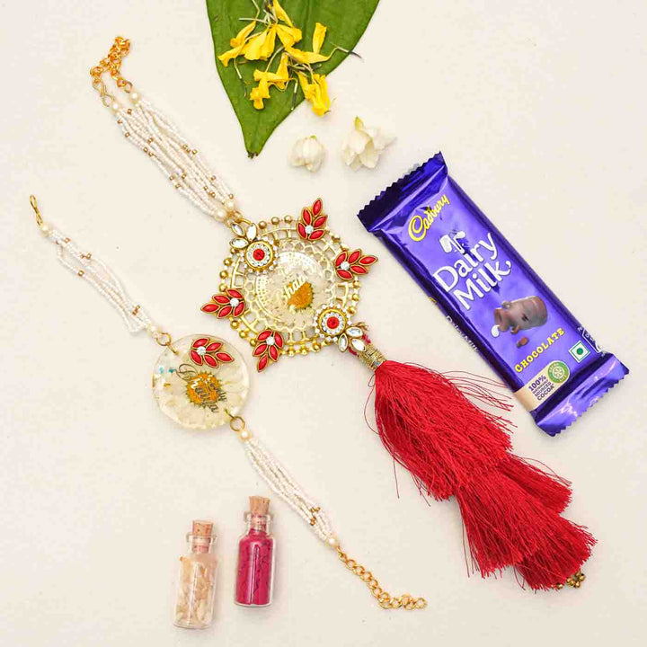 Handmade Resin Lovely Bhaiya And Lovely Bhabhi With Real Flower Rakhi With Chocolates And Roli Chawal Set Of 2 - Flat lay with gift items