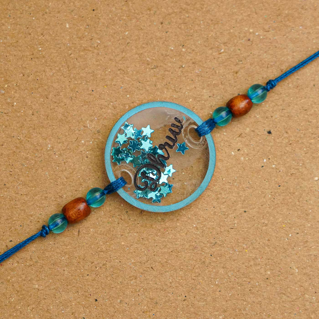 Personalized Handmade Round Glitter Acrylic Rakhi With Roli Chawal - Close-up of blue personalized name tag