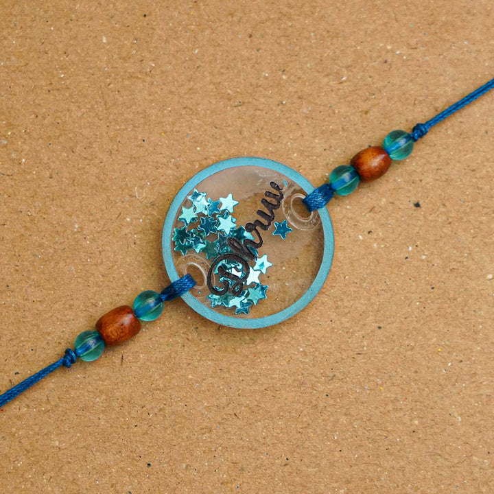 Personalized Handmade Round Glitter Acrylic Rakhi With Roli Chawal - Close-up of blue personalized name tag