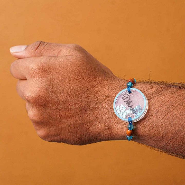 Personalized Handmade Round Glitter Acrylic Rakhi With Roli Chawal - Model wrist wearing blue bracelet