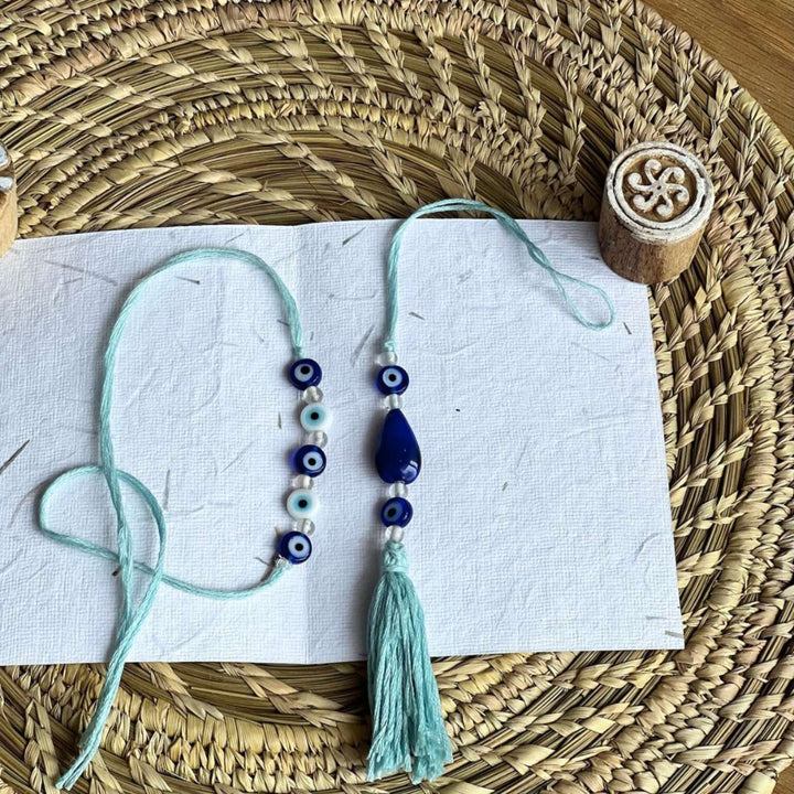 Handmade Beaded Evil Eye Jute Bhaiya Bhabhi Rakhi With Roli Chawal Set Of 2 - Flat Lay on Textured Mat