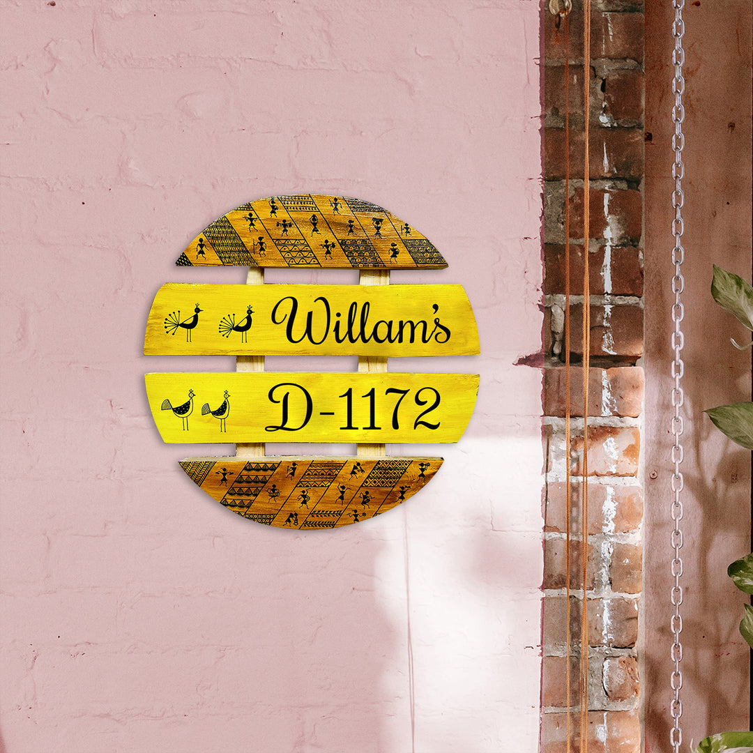 Handcrafted Personalized Warli Art Round Pinewood Name Plate - Mounted on Pink Wall Front View