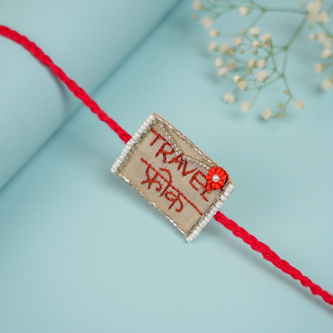 Handmade Beaded Travel Freak Rakhi With Roli Chawal For Brother - Angled view of Rakhi on blue background