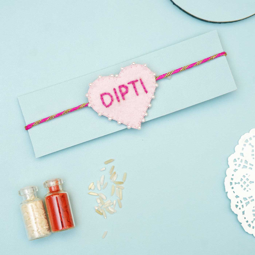 Personalized Handmade Pink Heart Felt Rakhi With Roli Chawal - Single rakhi on blue cardboard