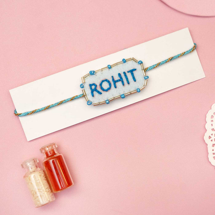Personalized Handmade Blue Rectangle Felt Rakhi With Roli Chawal - Displayed on Card Background