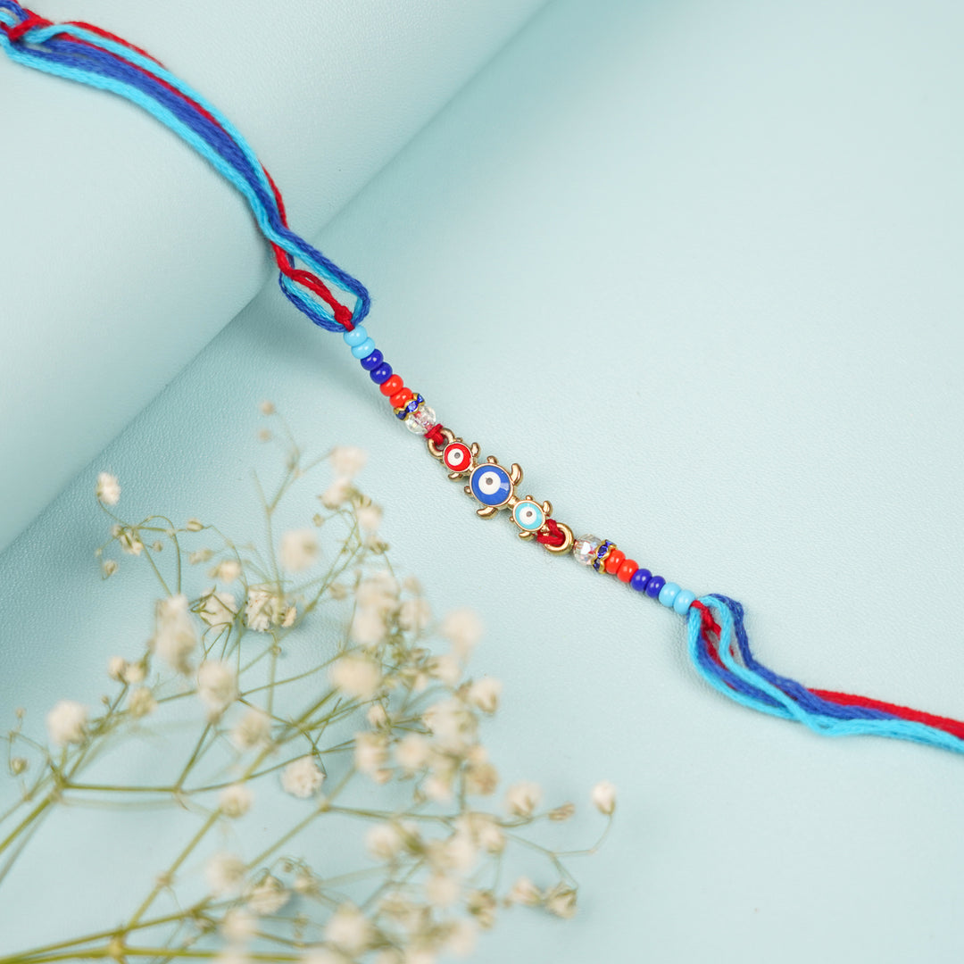 Handmade Beaded Turtle Evil Eye Rakhi With Roli Chawal - Flat Lay with Floral Accents
