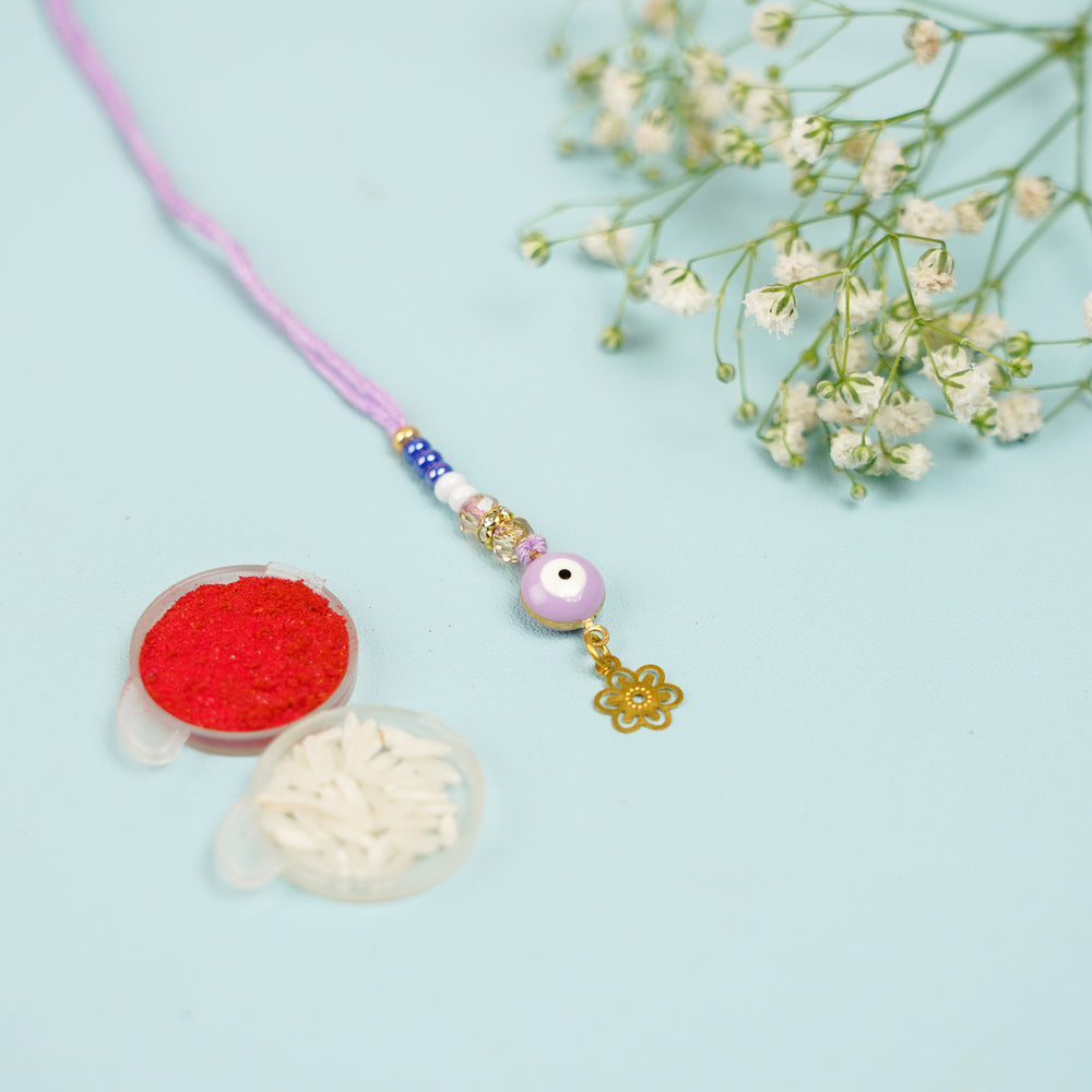 Handmade Yellow Evil Eye Lumba Rakhi For Bhabhi With Roli Chawal - Flat Lay with Tilak and Rice