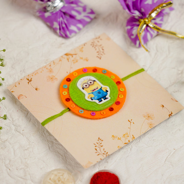 Handmade Minion Kids Rakhi With Roli Chawal - Angled View with Gift Elements
