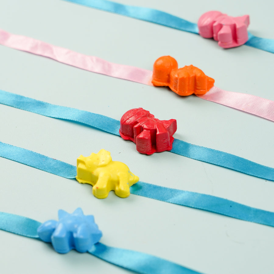 Reusable Non Toxic Multicolour Dino Theme Wax Kids Rakhi Set Of 5 - Flat Lay Display of Dinosaur Bracelets