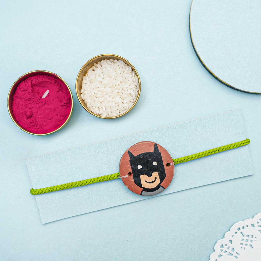 Hand Painted Batman Terracotta Rakhi With Roli Chawal For Kids - Charm Displayed with Decorative Items