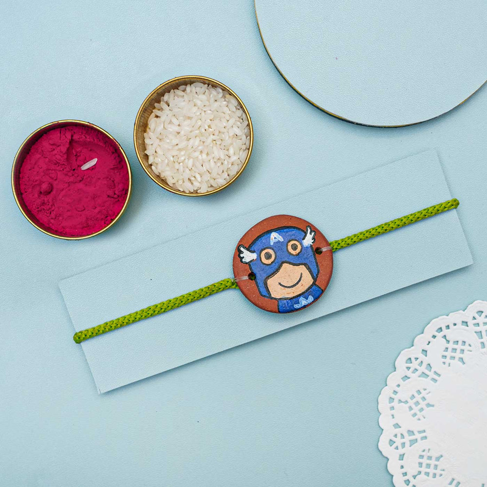 Hand Painted Captain America Terracotta Rakhi With Roli Chawal For Kids - Styled Presentation with Accessories