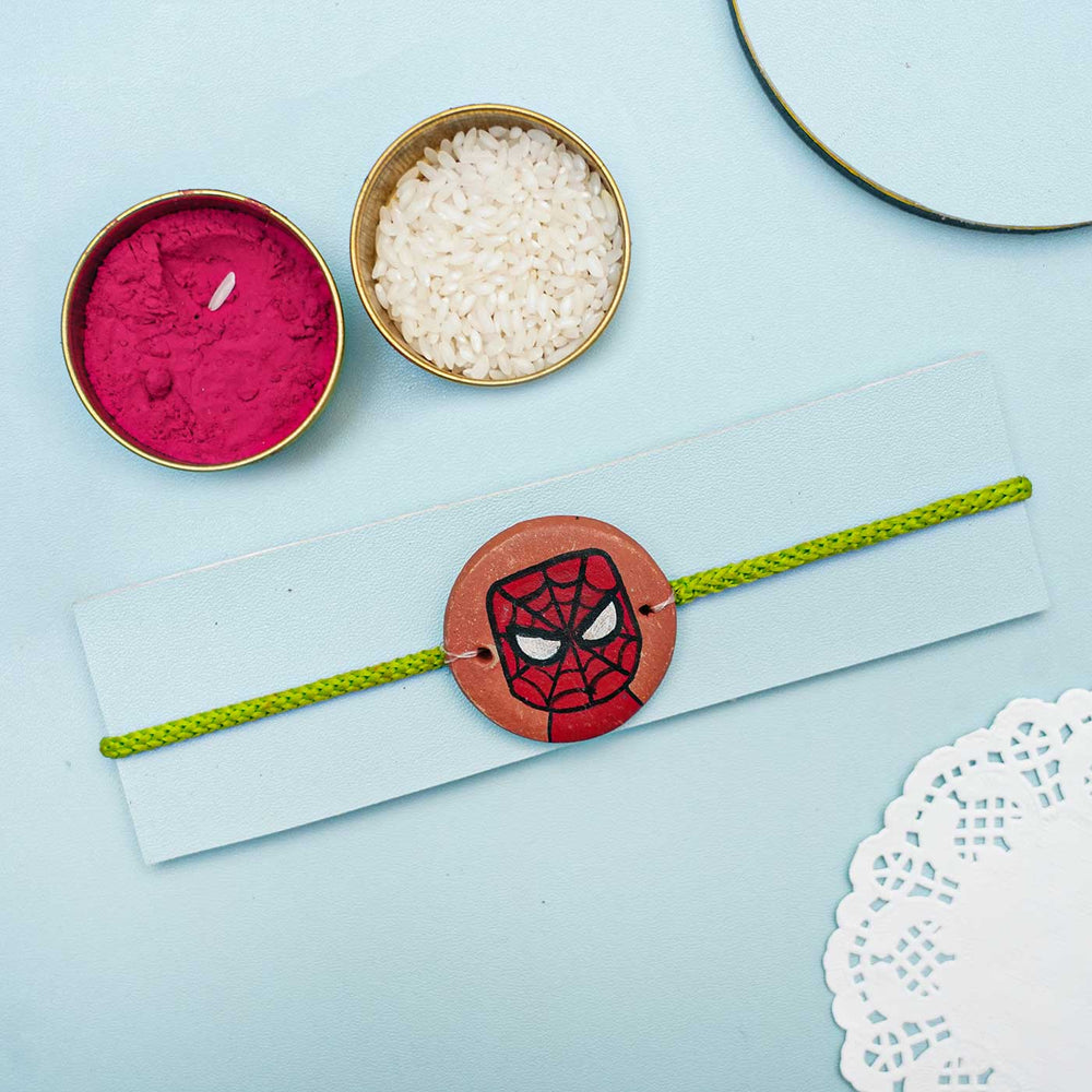 Hand Painted Spiderman Terracotta Rakhi With Roli Chawal For Kids - Styled display with ritual items and bracelet