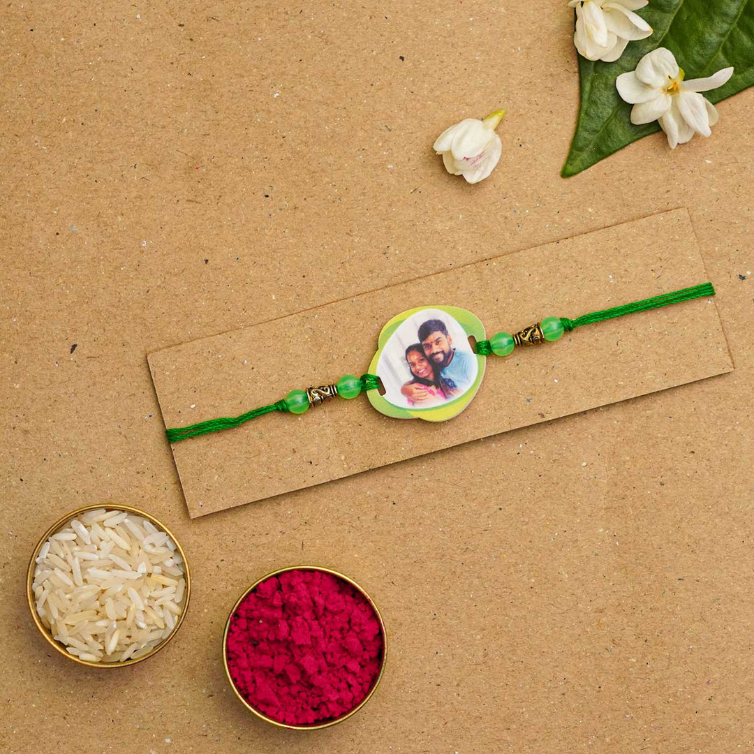 Photo Personalized Handmade Photo Acrylic Rakhi With Roli Chawal - Green rakhi displayed with traditional items